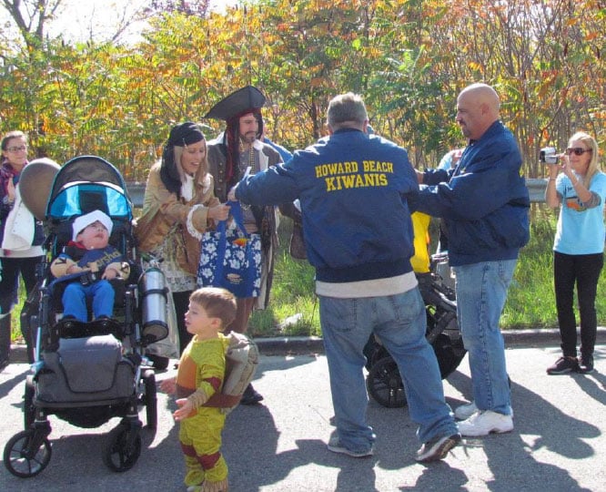 Group of people gathered outdoors, including individuals wearing Kiwanis jackets, assisting people in wheelchairs.