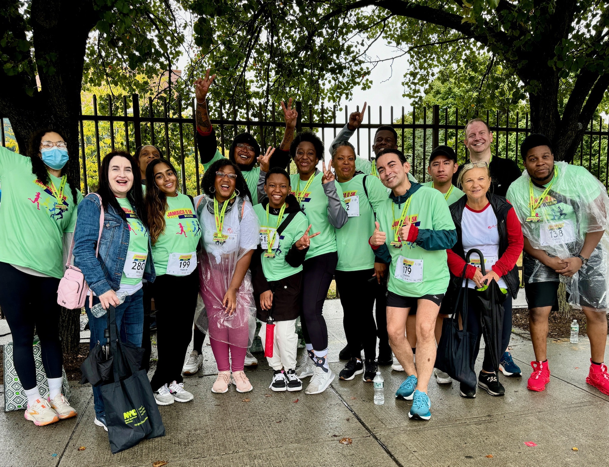 Group of people in green shirts standing together and smiling outside, under trees
