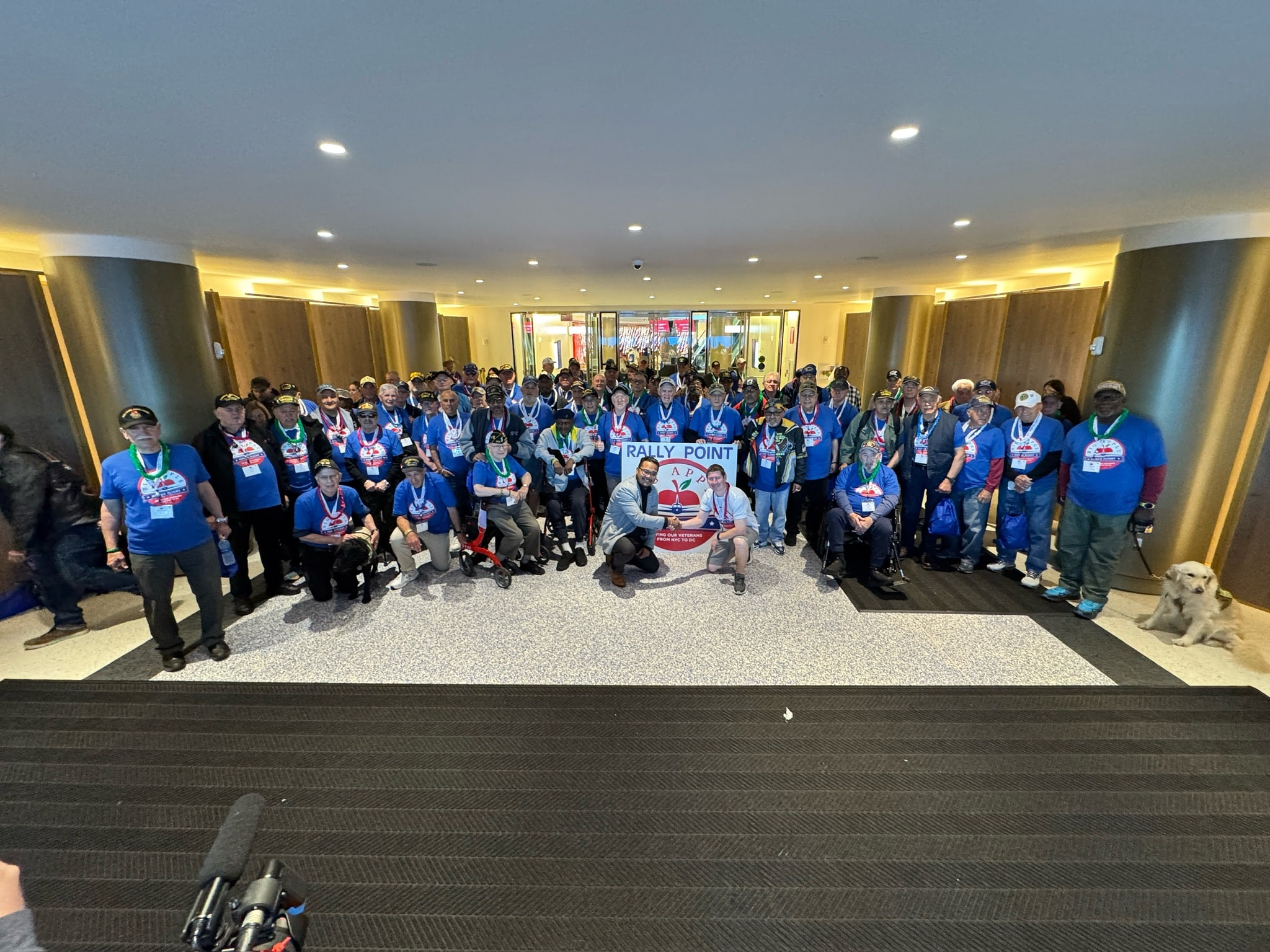 Large group of people in blue shirts posing for a photo, with "Rally Point" written on the floor behind them.