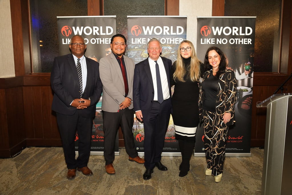 A group photo of five people posing in front of event banners that say "WORLD LIKE NO OTHER".