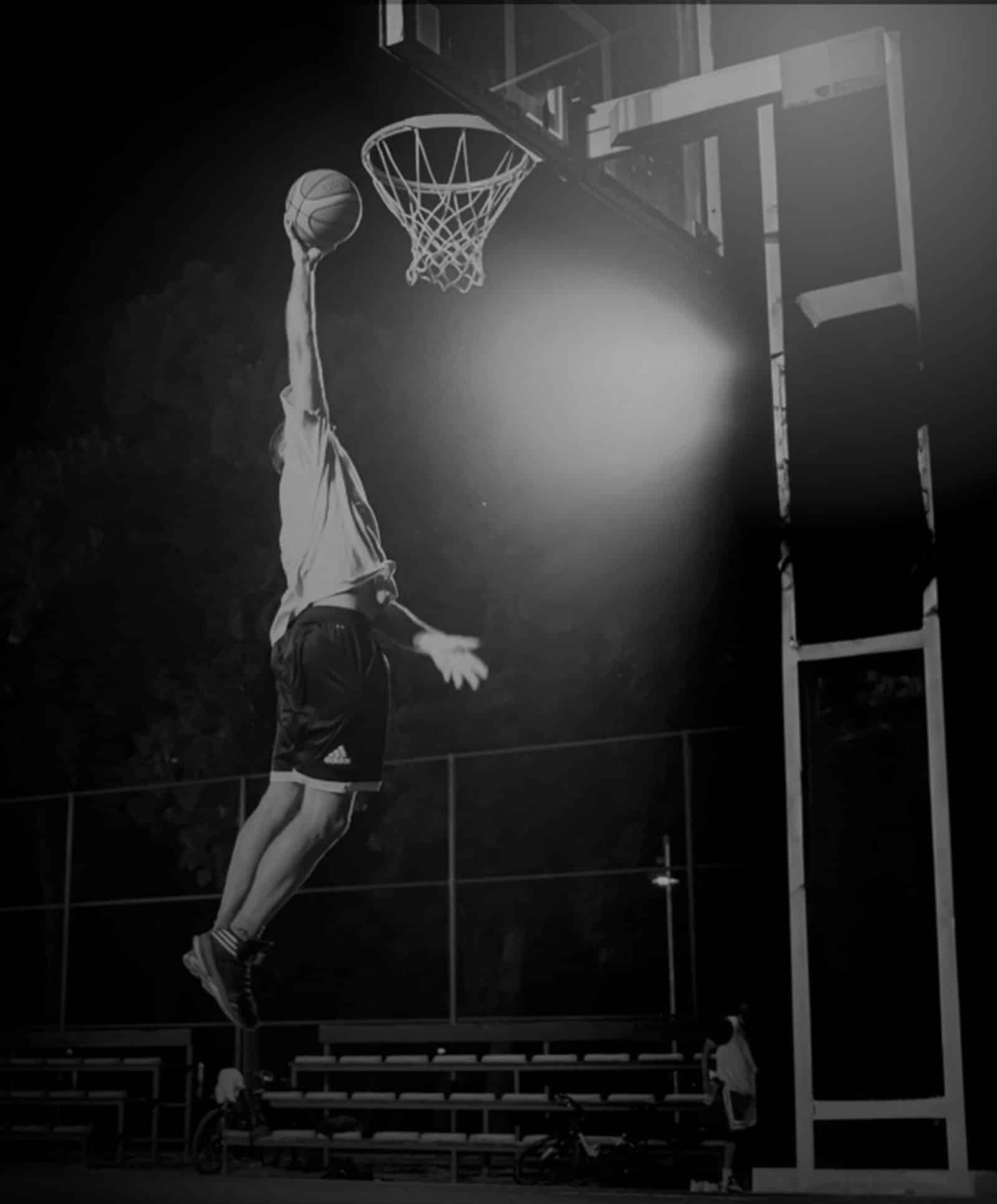 A basketball player mid-jump, reaching up to shoot the ball through a hoop on a basketball court.