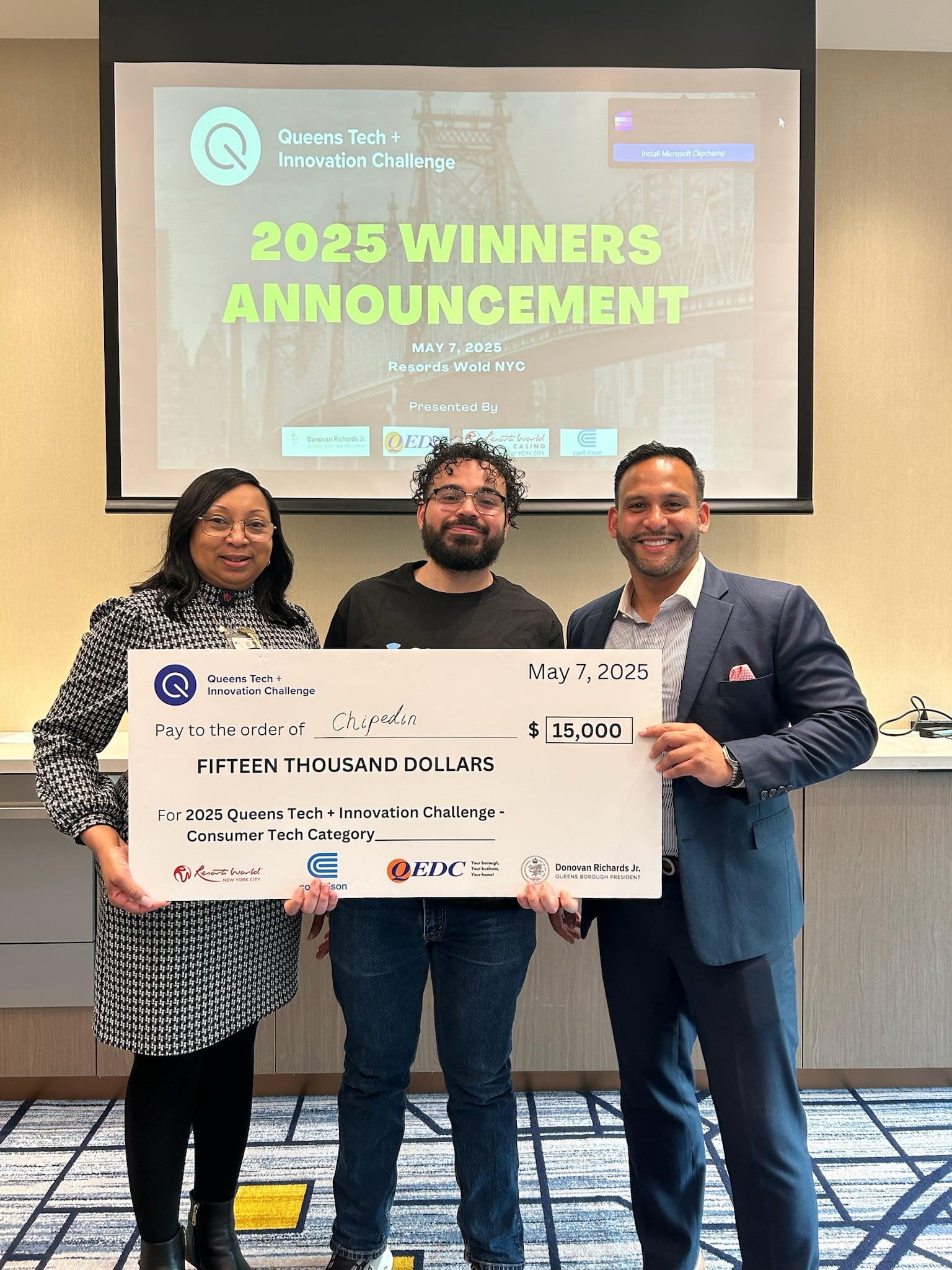 Three people holding a $15,000 award check for winning the Queens Tech + Innovation Challenge - Consumer Tech Category.