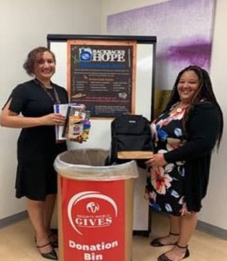 Two women standing next to a donation bin and framed 'Words of Hope' poster.