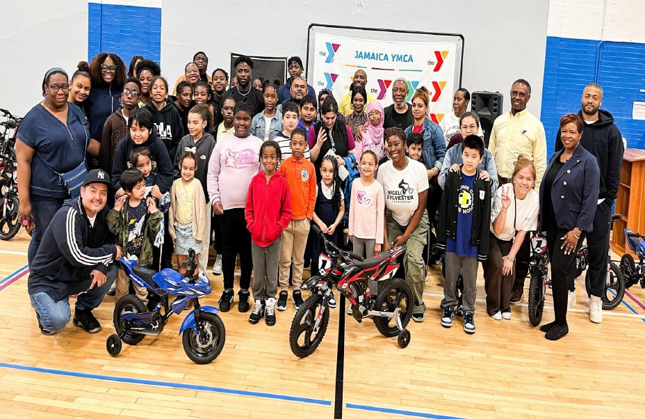 Group photo of community members gathered in a YMCA facility, with a YMCA sign visible and people of diverse ages and backgrounds posing together.