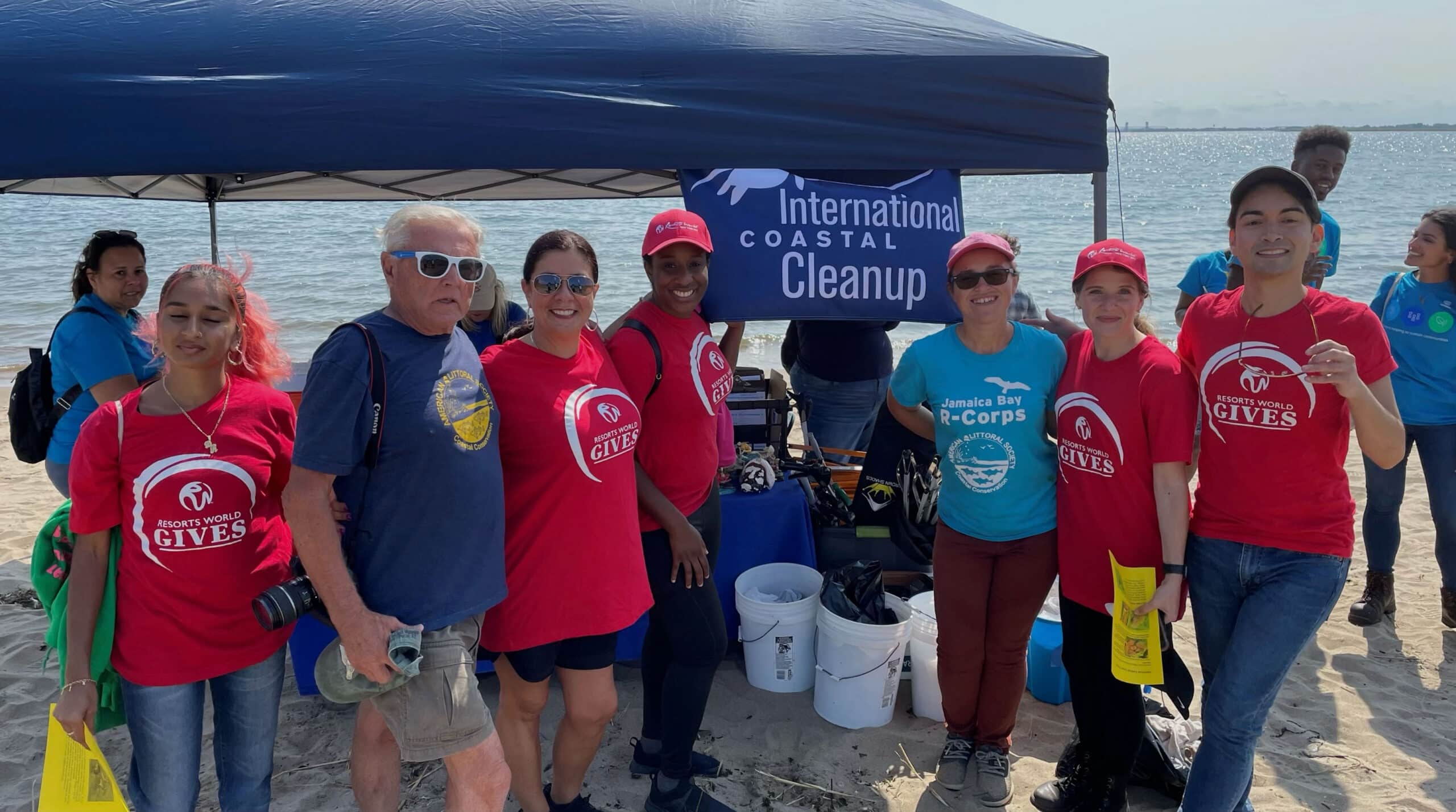 A group of people wearing International Coastal Cleanup branded red and blue shirts, standing in front of a large tent with the organization's logo displayed.