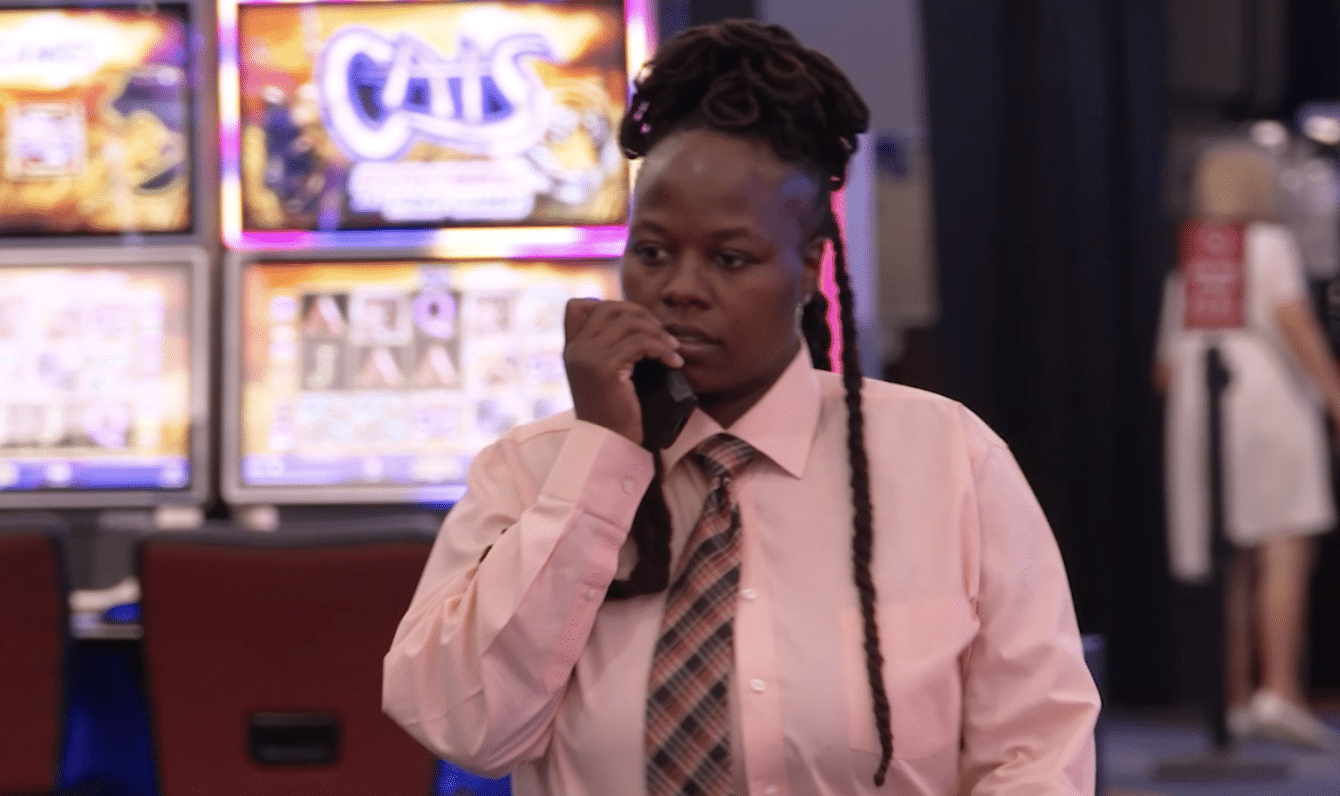 A person wearing a white shirt and tie, with braided hair, speaking into a microphone in front of a sign that says "Cain's".