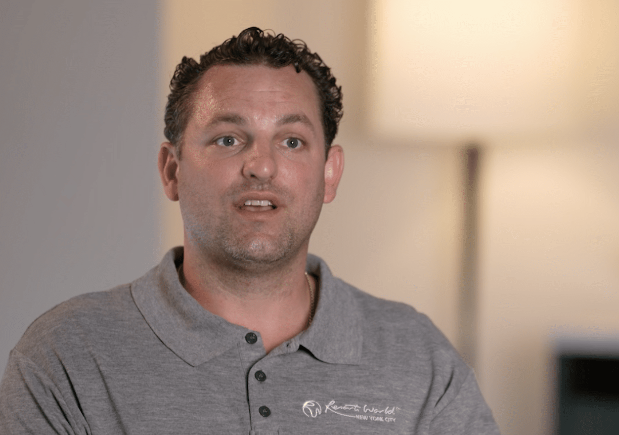 A man with curly hair wearing a gray polo shirt with "Kenneth Cole" logo.