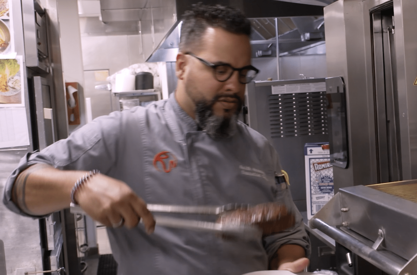 A man in a gray kitchen uniform checking the equipment in an industrial kitchen.