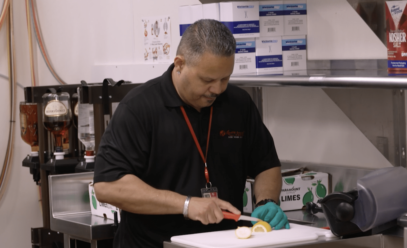 A person in a black uniform cutting a lemon on a cutting board in a commercial kitchen setting.