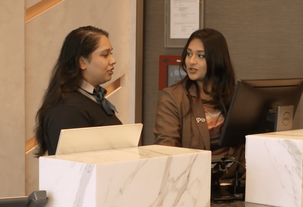 Two women in business attire conversing at a hotel reception desk
